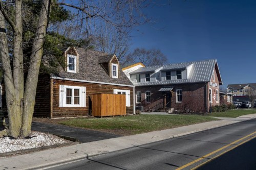 Two houses side by side: a rustic wooden cabin and a modern brick home, set against a clear blue sky.