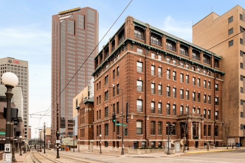 Historic brick building in the foreground with modern skyscrapers in the background, set in an urban environment.