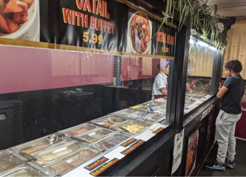 A buffet counter with various dishes, a chef serving food, and a customer observing the selection.