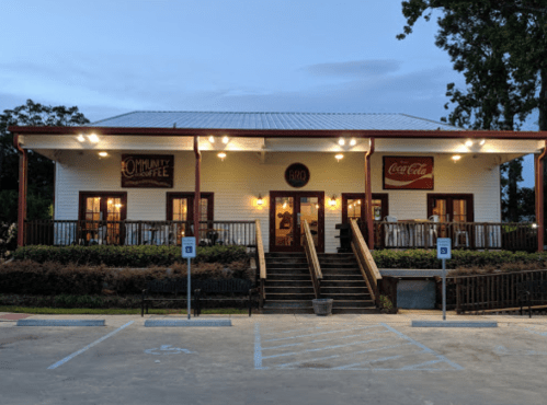 A charming restaurant with a porch, illuminated at dusk, featuring signs for Coca-Cola and a local community event.