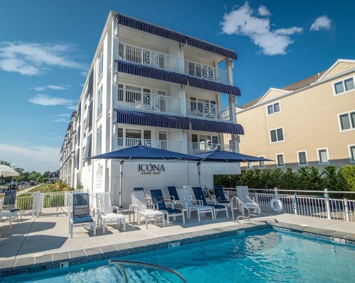 A modern hotel with blue awnings, a pool area, and lounge chairs under a clear blue sky.
