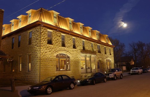Historic stone building with a copper roof, illuminated at night under a full moon, with parked cars in front.