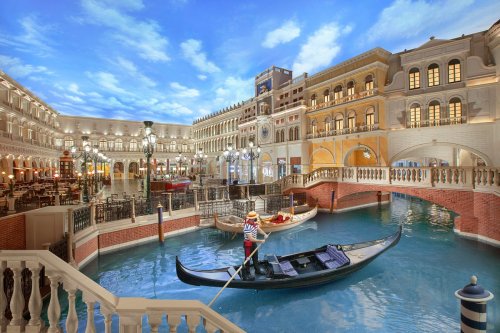 A scenic view of a Venetian-style canal with a gondola and ornate buildings under a blue sky.