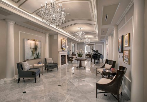 Elegant lobby with marble floors, chandeliers, and a grand piano, featuring stylish seating and decorative artwork.
