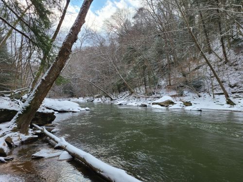 A serene river scene with snow-covered banks and trees, reflecting a peaceful winter landscape.
