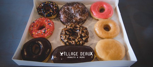 A box of nine assorted donuts, featuring chocolate, sprinkles, and glazed varieties.