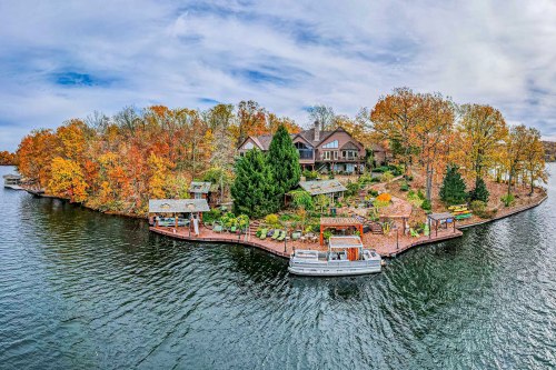 Aerial view of a lakeside property surrounded by autumn foliage, featuring a boat and landscaped gardens.