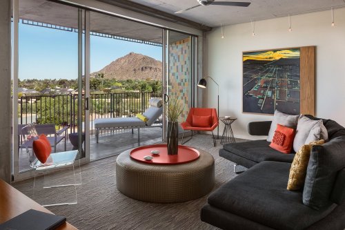 Modern living room with a view of a mountain, featuring a sectional sofa, colorful decor, and large glass doors.