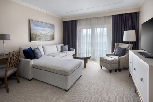A modern hotel room featuring a gray sofa, armchair, coffee table, and large window with sheer curtains.
