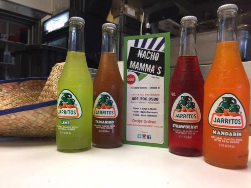 Four bottles of Jarritos soda in lime, tamarind, strawberry, and mandarin flavors, next to a menu for Nacho Mamma's.
