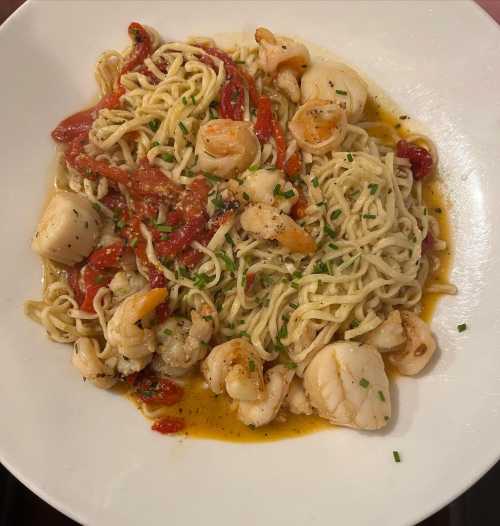 A plate of pasta with shrimp, scallops, and red peppers in a light sauce, garnished with chopped herbs.