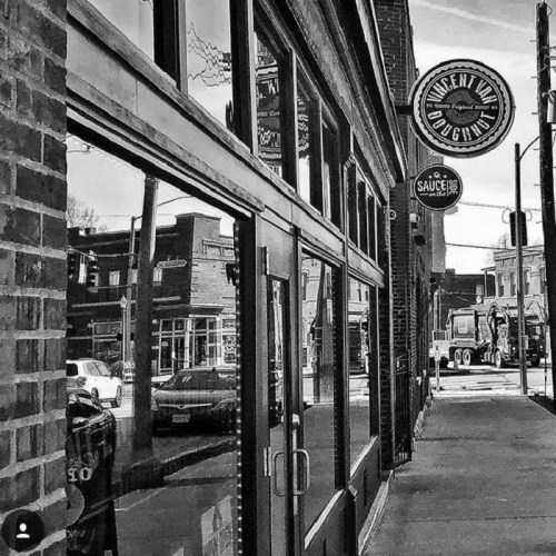 Black and white street view featuring a doughnut shop and reflections of nearby buildings and vehicles.