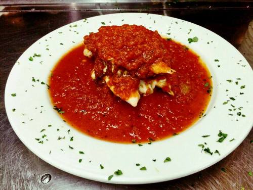 A plate of lasagna topped with marinara sauce and garnished with parsley, served in a pool of sauce.