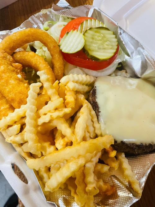 A takeout container with a cheeseburger, crinkle-cut fries, onion rings, and a side salad with tomatoes and pickles.