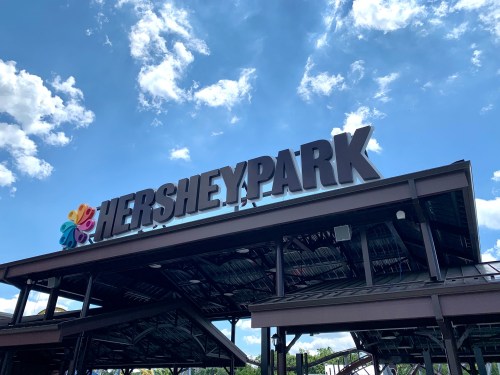 Sign for Hersheypark under a blue sky with clouds, featuring colorful elements on the left side.