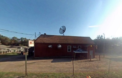 A red building with a large satellite dish on the roof, surrounded by a gravel area and a blue canopy.