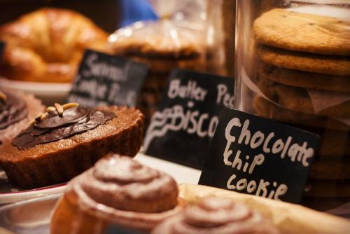 A display of assorted baked goods, including chocolate chip cookies, muffins, and pastries, with handwritten labels.