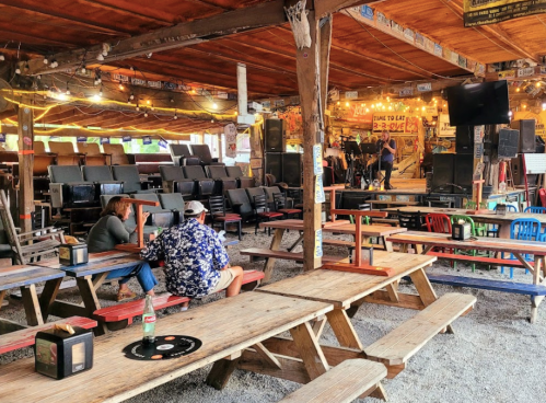 A rustic venue with wooden tables and chairs, featuring a stage and colorful decor, set for a live performance.