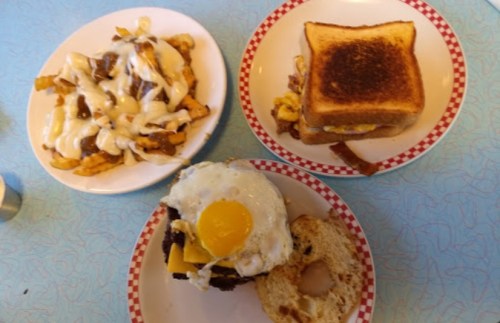 Three plates of food: loaded fries with cheese, a toasted sandwich, and a bagel topped with an egg and cheese.