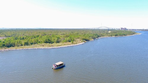 Aerial view of a river with a small boat and lush greenery along the banks under a clear blue sky.