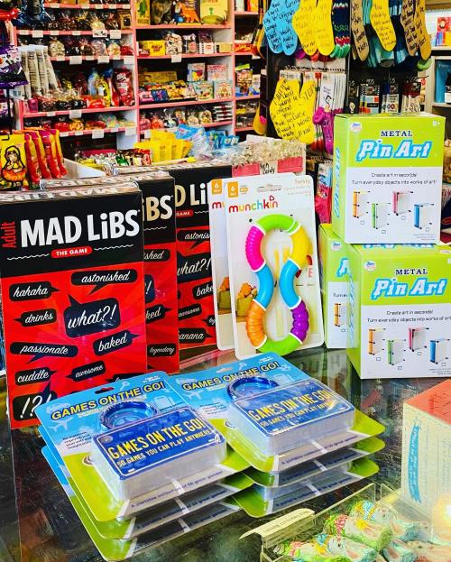 A colorful display of games and toys, including Mad Libs, Munchkin, and Metal Pin Art, in a vibrant store setting.