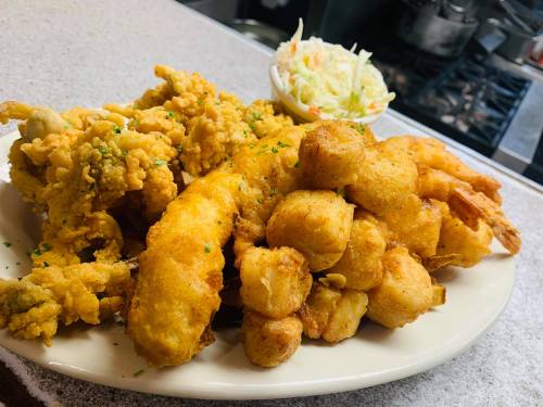 A plate of fried seafood, including shrimp and fish, served with a side of coleslaw.