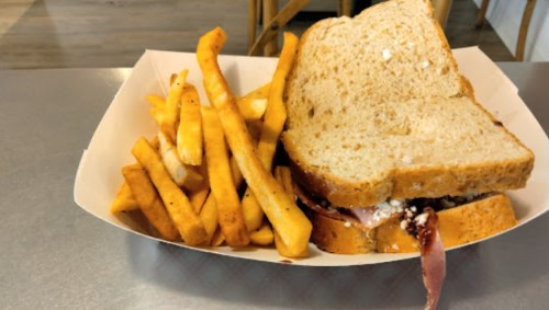 A sandwich on whole grain bread with a side of golden French fries in a paper tray.