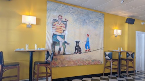 A colorful mural of a man walking a dog with a child, set against a bright yellow wall in a dining area.