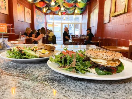Two plates of food on a granite table, featuring sandwiches and a side salad, in a colorful restaurant interior.
