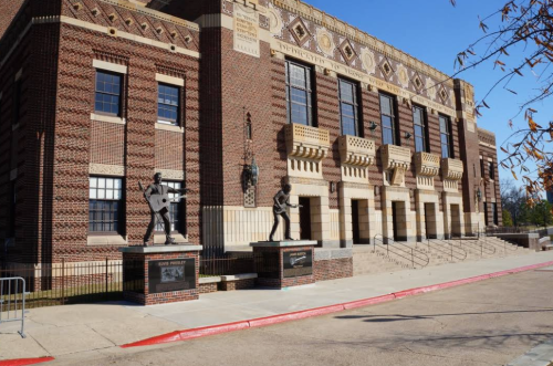 Exterior view of a historic building with two statues of musicians in front, surrounded by trees and a clear blue sky.