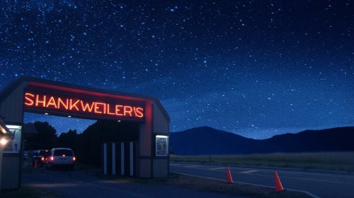 A brightly lit sign for Shankweilers under a starry night sky, with mountains in the background and a car parked nearby.