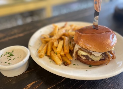A juicy burger with melted cheese and grilled onions, served with fries and a small bowl of dipping sauce.
