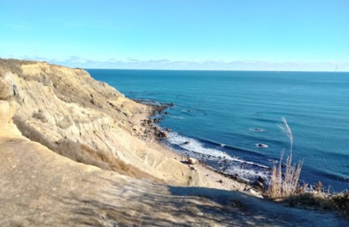 A scenic view of a rocky coastline with calm blue waters and a clear sky.