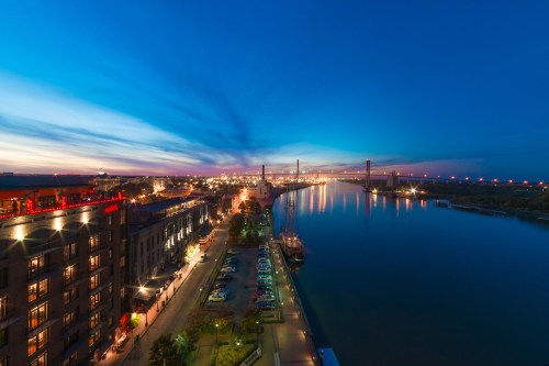 A scenic view of a river at dusk, with city lights reflecting on the water and a bridge in the background.