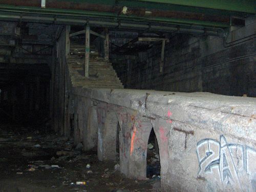 Abandoned underground space with stone steps, graffiti on walls, and debris scattered on the ground.