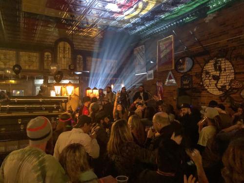 A lively bar scene with a crowd enjoying live music, colorful lights, and a festive atmosphere.