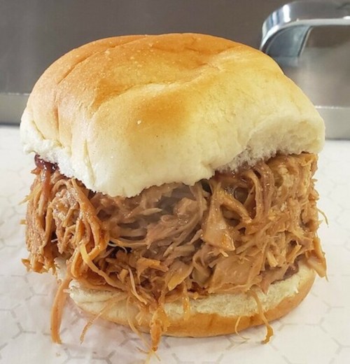 A close-up of a pulled pork sandwich on a soft bun, filled with shredded meat and a hint of barbecue sauce.