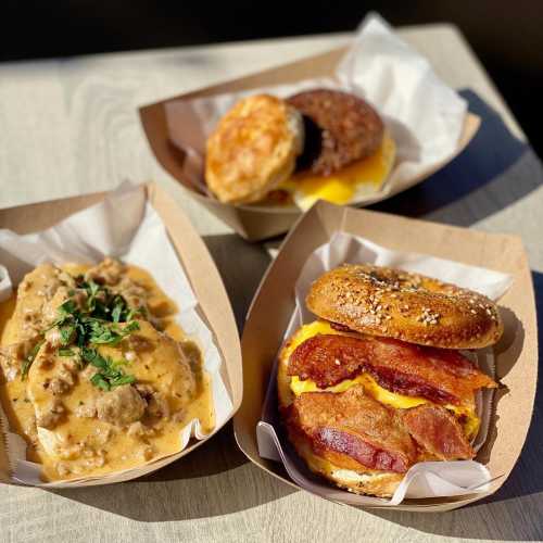 Three breakfast dishes: a biscuit with gravy, a sandwich with bacon and cheese, and a biscuit with sausage.