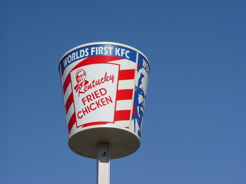 Sign for the world's first KFC, featuring a bucket design and the text "Kentucky Fried Chicken" against a blue sky.