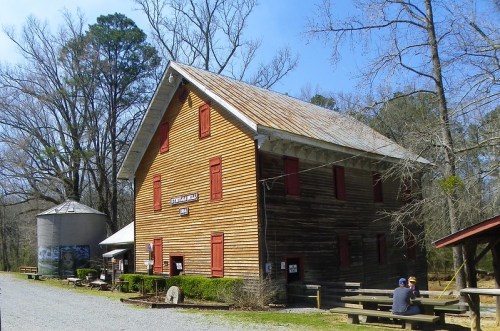 A rustic wooden building with red shutters, surrounded by trees, and a picnic area in front. A silo is nearby.