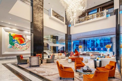 Modern hotel lobby featuring elegant decor, vibrant artwork, plush seating, and a stunning chandelier.
