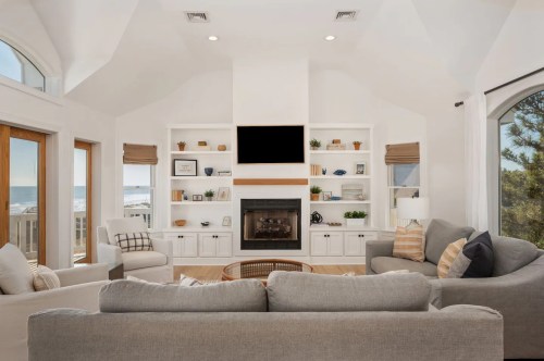 Bright living room with large windows, a fireplace, and built-in shelves, featuring cozy furniture and ocean views.