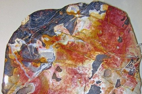 A colorful slab of polished stone featuring swirls of red, orange, black, and white patterns.