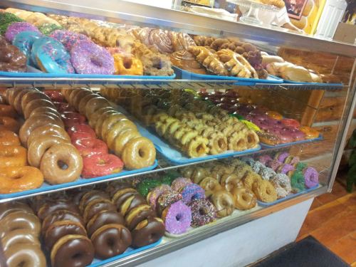 A display case filled with a variety of colorful donuts, including glazed, frosted, and sprinkled options.