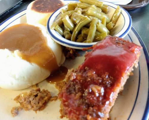 A plate featuring meatloaf with ketchup, mashed potatoes with gravy, and a side of green beans.