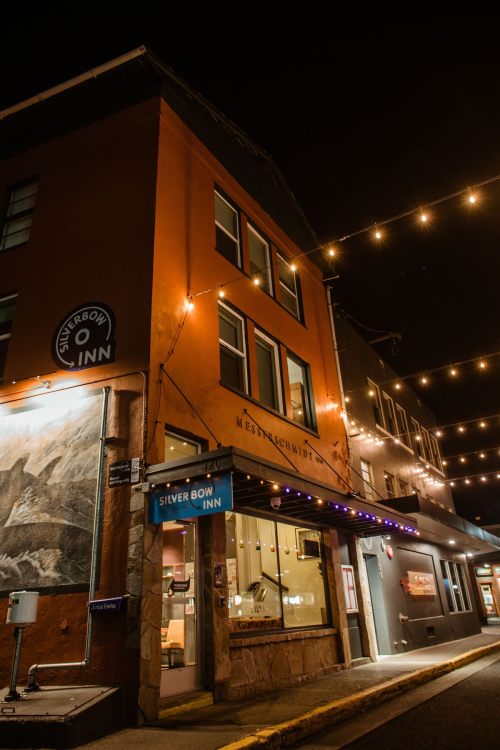 A cozy inn at night, illuminated by string lights, with a warm orange facade and a welcoming entrance.