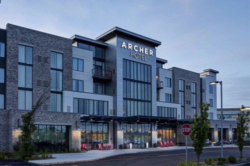 Modern Archer Hotel exterior with large windows, stone accents, and a welcoming entrance at dusk.