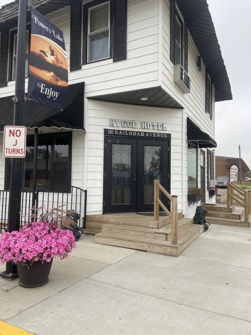 Exterior of the Hygge Hotel on Railroad Avenue, featuring a sign and flower planters at the entrance.