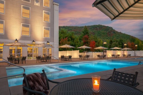 A serene pool area with lounge chairs and umbrellas, surrounded by trees, under a colorful sunset sky.