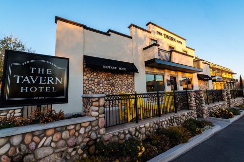 Exterior of The Tavern Hotel, featuring a stone facade, large windows, and a sign indicating it's a boutique hotel.